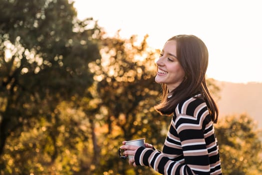 young woman smiling happy with hot drink in nature