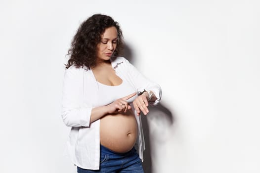 Isolated portrait on white background of curly haired expectant woman counting contractions on her smart wrist watch
