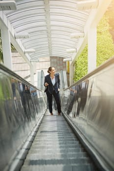 On her way up to the office. a young businesswoman using a cellphone on an escalator.