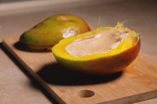 Mango. Close-up of fresh mango fruit cut in half on wooden cutting board and table background