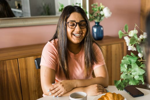 Portrait of joyful diversity indian woman enjoying a cup of coffee at home. Excited woman wearing spectacles and laughing