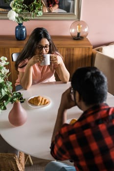 Young diverse loving couple eating croissant and talks together at home in breakfast time. Communication and relationship concept