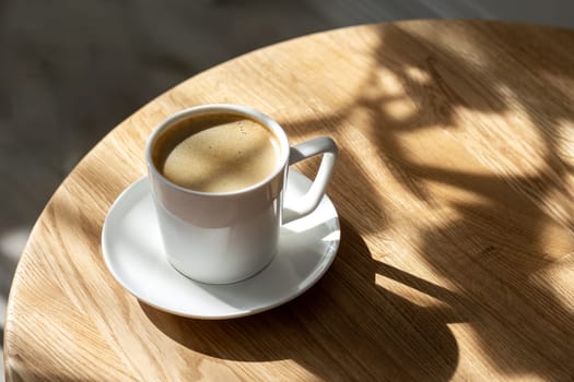 A white porcelain cup with coffee on a saucer stands on a round table