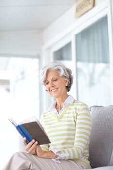 Books can take you anywhere. a happy senior woman reading a book on the sofa at home.