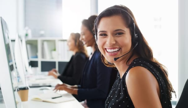 For any questions you might have, give us a call. a young woman using a computer and headset in a modern office.