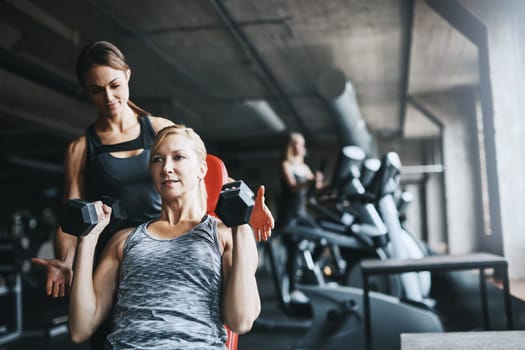 Think about the results you want. a mature woman lifting weights with a female instructor at the gym.
