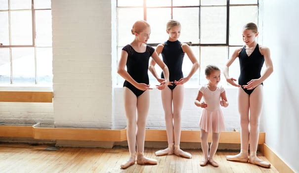 Showing her the way of ballet. a group of young ballerinas teaching a little girl ballet in a dance studio.