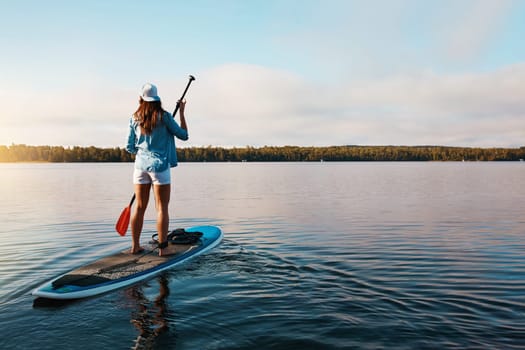 Im doing something for me. a young woman paddle boarding on a lake.