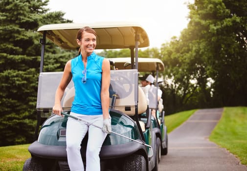 The end is in sight. an attractive young woman leaning against a golf cart on a golf course.
