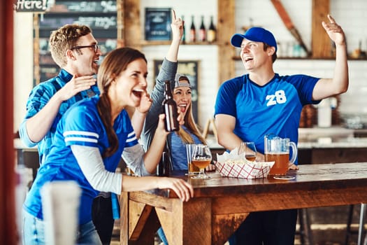 Sporty fun with friends. a group of friends cheering while watching a sports game at a bar.