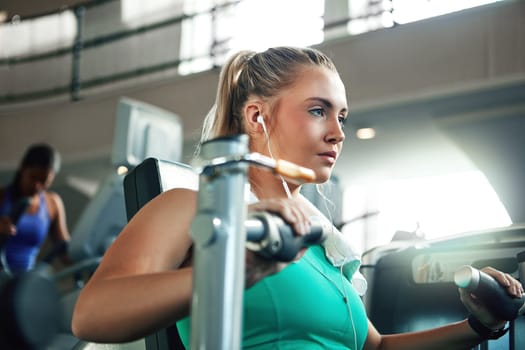 Nothing comes between her and a gym session. a young woman working out with a chest press at a gym.