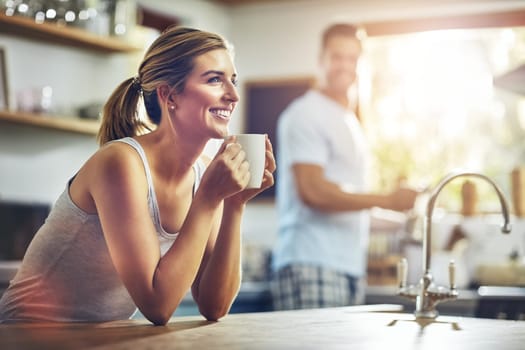 Coffee is instant happiness. a young woman having her morning coffee with her boyfriend standing in the background.