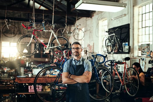 Striving to provide superior bicycle repair service. Portrait of a mature man working in a bicycle repair shop with his coworker in the background.