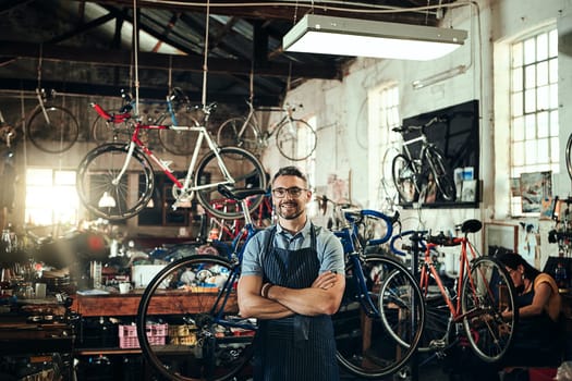 Your bicycle is always welcome here. Portrait of a mature man working in a bicycle repair shop with his coworker in the background.