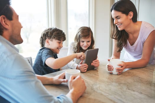 Finding fun on the world wide web. a married couple and their young children playing with a tablet together in their kitchen.