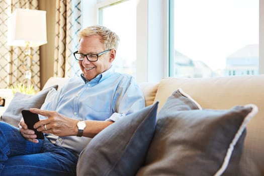 Getting a smartphone was the best decision he made. a mature man using a phone at home on the sofa.