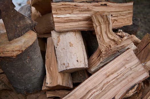 Still life. A heap of wood for making fire. Partial view of a hatchet in a stump near firewood in rustic background.