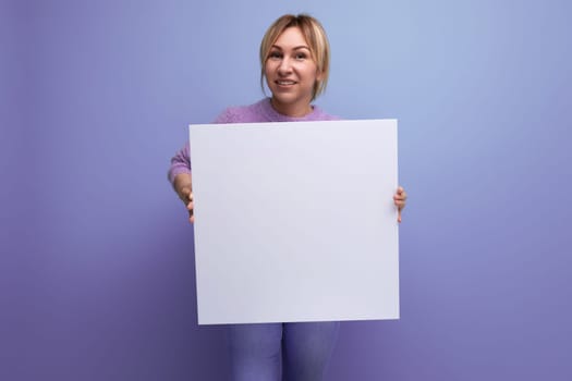 attractive blond woman holding a sheet of paper with a mockup for a promotion message on a purple background