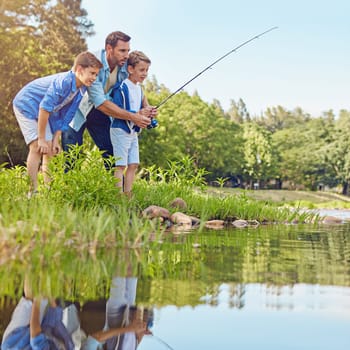 Teaching his boys how to fish. a father and his two sons out fishing in the woods.