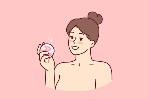 Woman with bath bomb in hands smiles as she prepares to take bath with aromatic substances