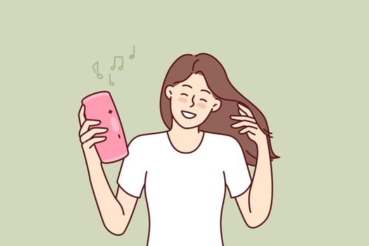 Woman with wireless portable speaker smiling enjoying loud rhythmic music of favorite rock band