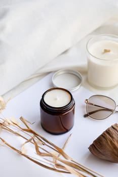 Soy wax aroma candle in brown jar on bed , with fashion glasses. Candle mockup design