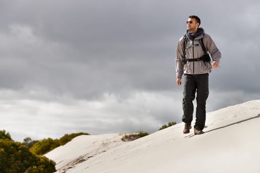 He handles these hills like a seasoned hiker. a young male hiker walking along the sand dunes.