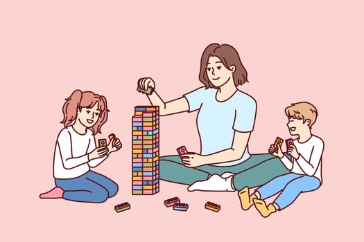 Woman babysitter with kids plays constructor building tower of children blocks in kindergarten