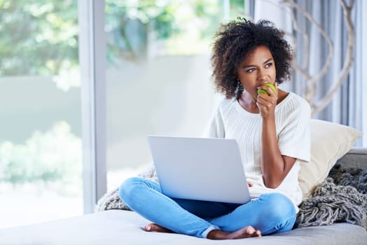 Munching on some healthy snacks while web browsing. a young woman eating an apple while using her laptop at home.