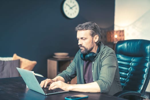 Man sitting at desk home, typing on laptop and chatting online through messaging app. He dressed in casual clothing and surrounded by technology, with wireless mobile phone router visible in the background. This image is perfect for representing remote work, telecommuting, or the modern workplace.