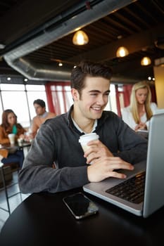 Updating his social media profile. A handsome young man using his laptop in a coffee shop.