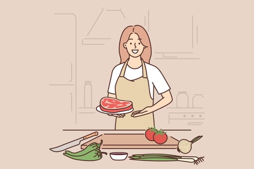 Woman cook holding raw meat steak standing near kitchen table with cutting board and vegetables