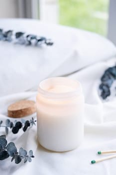 Soy wax aroma candle in white jar on bed with eucalyptus leaves. Candle mockup design