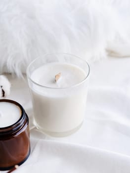 Soy wax aroma candle in white jar on bed with cotton branch. Candle mockup design