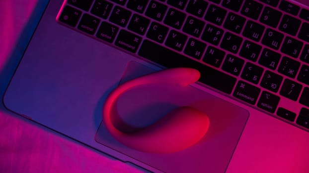 Close-up of a curved vibrator on a laptop keyboard in blue-red light.