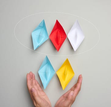 Two yellow-blue paper boats in female palms on a gray background. Ukraine support concept