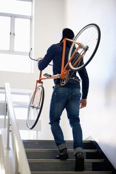 Really getting some exercise on the way to work. a trendy young man carrying his bicycle up a staircase indoors.