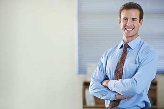 Climbing the corporate ladder. A young businessman standing and smiling with his arms folded - copyspace.