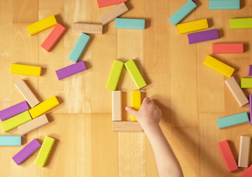 Child plays with colorful toy blocks on the ground in the flat. Educational game for children.