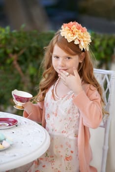 Being a lady...A red headed little girl dressed up and having a tea party in her garden.