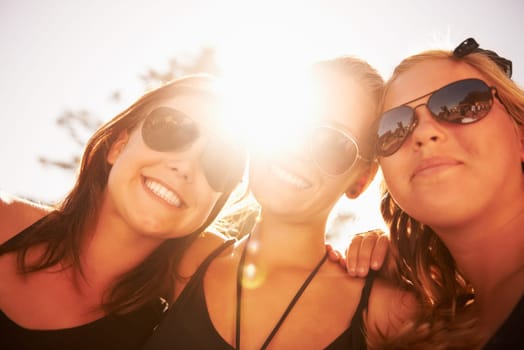 Good times together. Three friends hugging and smiling against a bright sky.