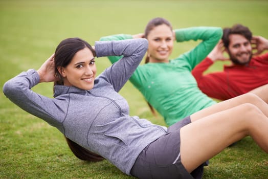 Working out together makes us push ourselves more. Portrait of three friends doing sit-ups together on a sports field.
