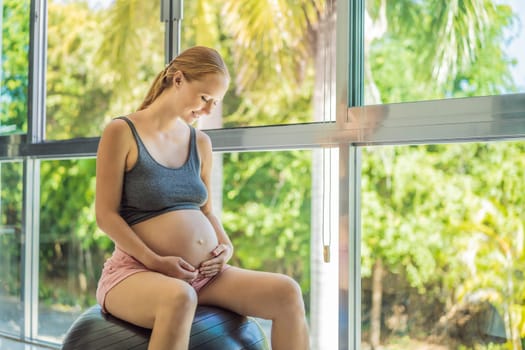 Pregnant woman exercising on fitball at home. Pregnant woman doing relax exercises with a fitness pilates ball. Against the background of the window