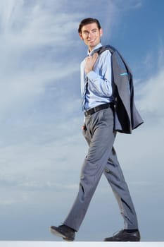 Ambition will take him far. Full body of a young businessman with his jacket over his shoulder against a blue sky.