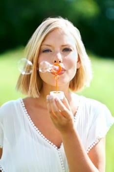 Its lifes simply pleasures that count. Lovely young woman blowing soap bubbles outdoors.