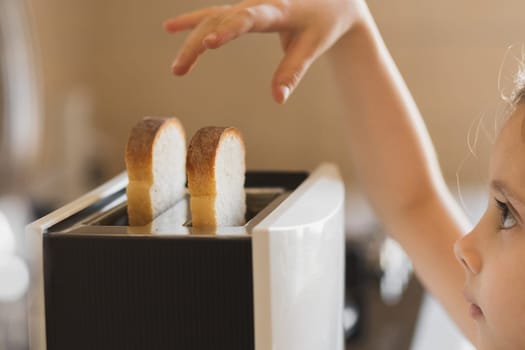 Close-up of a 5-7 year old girl who is preparing breakfast from toast in a toaster