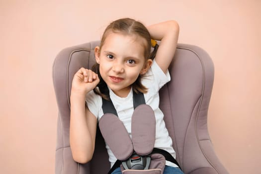 Funny smiling Caucasian preschool girl sitting in car seat looking at camera
