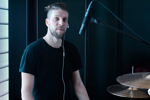 Portrait of a caucasian bearded drummer on a black stage behind a drum kit