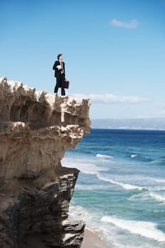 I can conquer the world. Young businessman holding a briefcase and a book standing on the edge of a cliff overlooking the ocean.