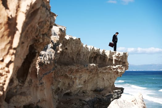 Its a long way down...Businessman holding a briefcase standing on a cliff looking down towards the ocean.